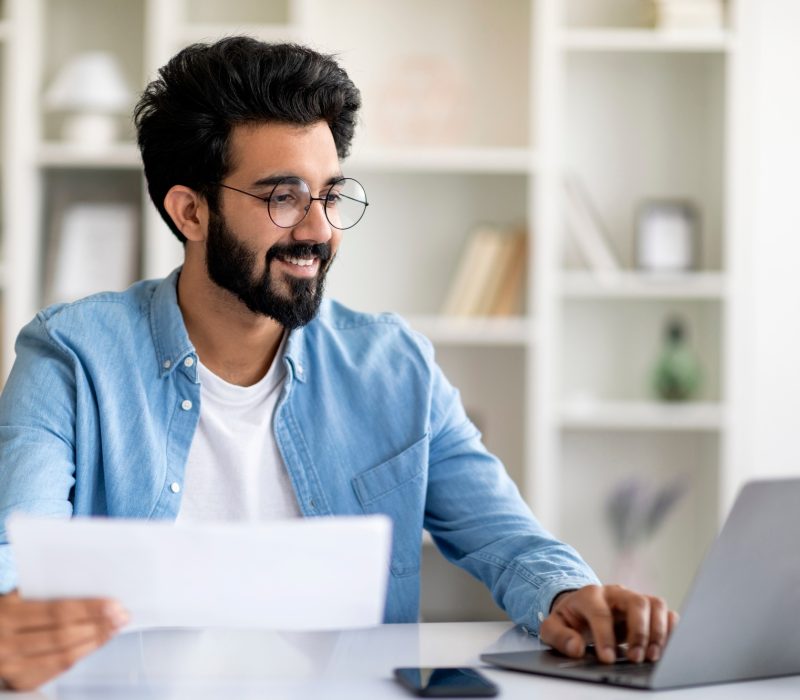 Indian Man Working With Papers And Laptop At Home Office